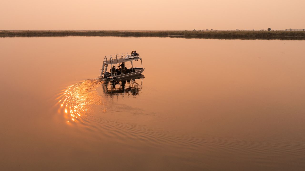 Romantic couple on top deck during golden red sunset river cruise on the Okavango Delta at Sitatunga Private Island, Botswana.