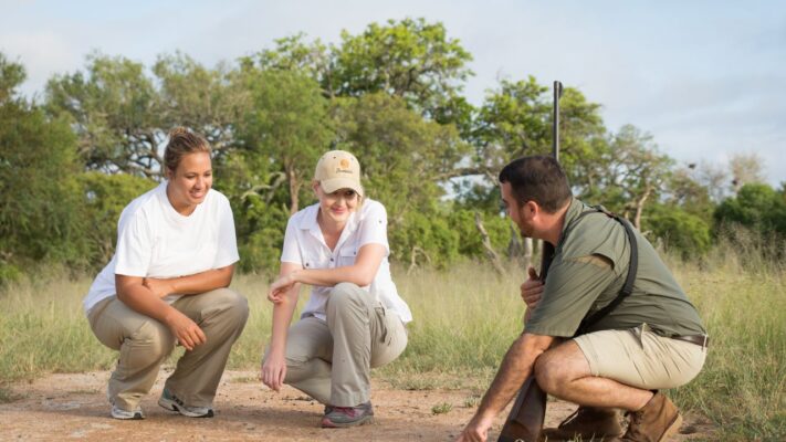 Ranger explaining animal footprints to guests crouched on walking safari in Kruger