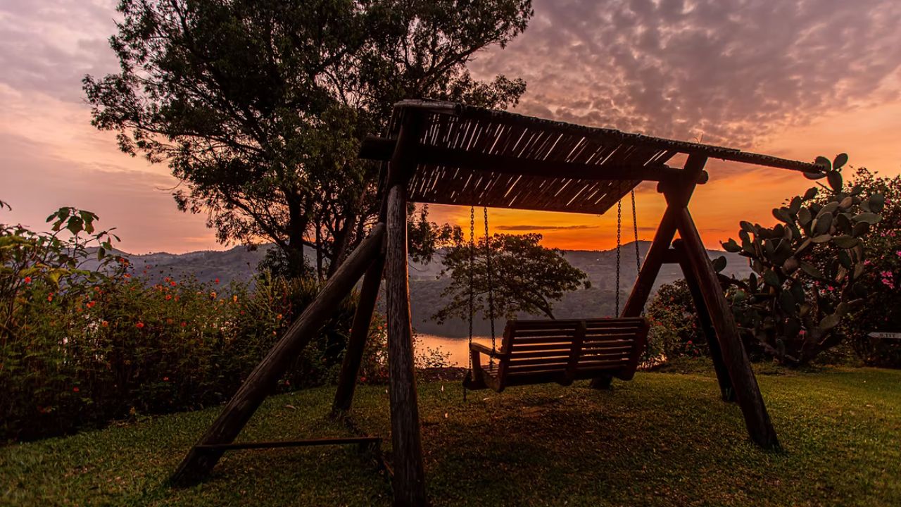 Wooden swing chair at sunset overlooking crater lake and jungle hills at Ndali Lodge.