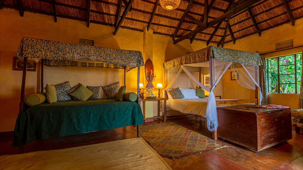 Double bed with soft lighting inside thatched guest room at Ndali Lodge Uganda.
