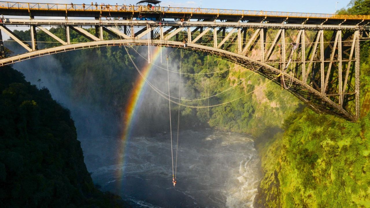 Bungee jumper leaping off Victoria Falls Bridge Zimbabwe with rainbow mist