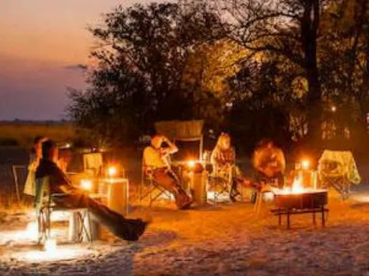 Group of people sitting around a campfire enjoying the African sunset on a Zambian horseback safari.