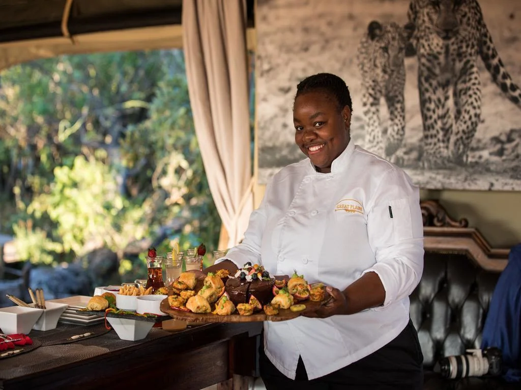 Staff waitress serving fruit platter in chef's uniform at safari camp lodge in Botswana.