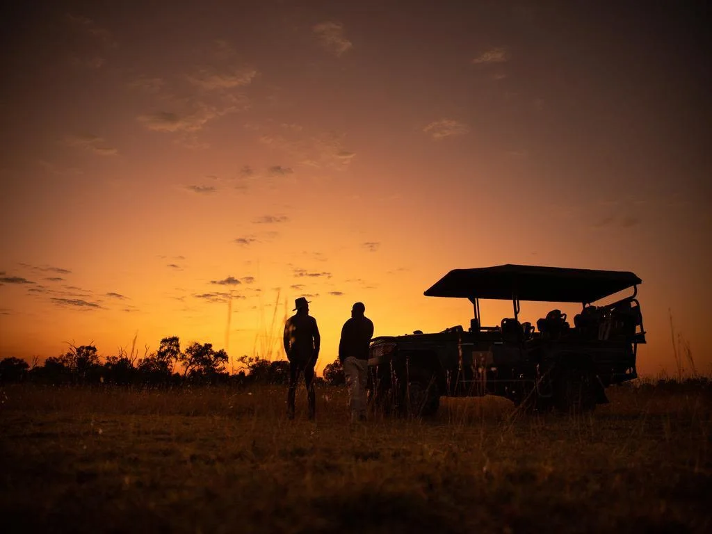 Silhouette of a Safari Guide and guest enjoying the African sunset in Botswana standing next to a game vehicle