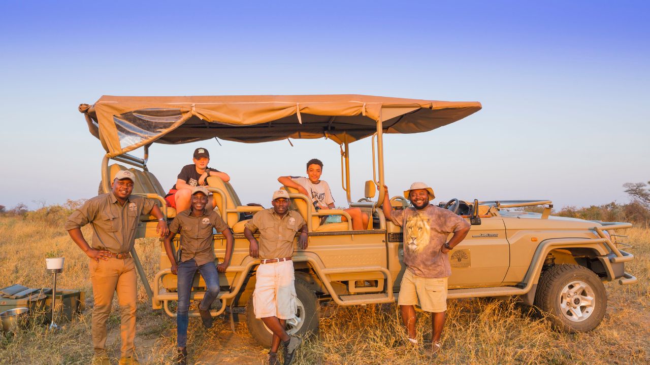 Game rangers and guests pose with orange sunset backdrop, Hwange