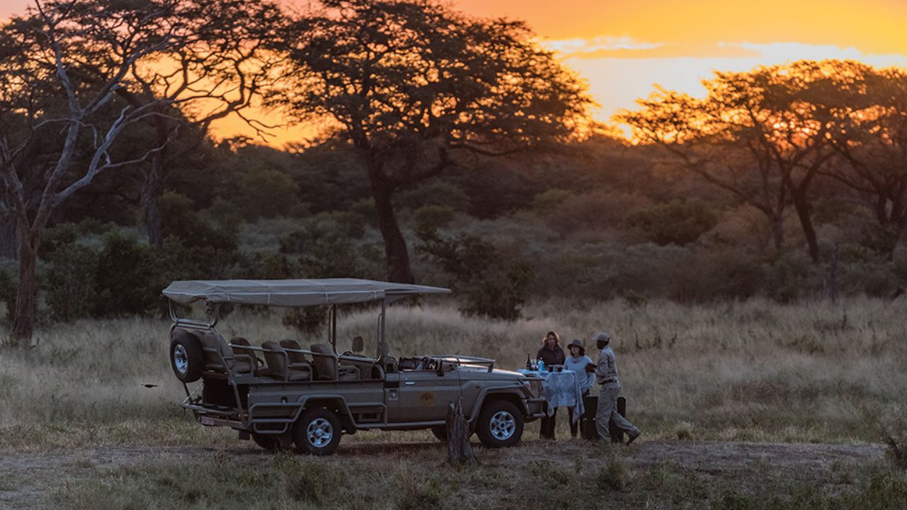 Guests on sunset game drive enjoying drinks, red African sunset