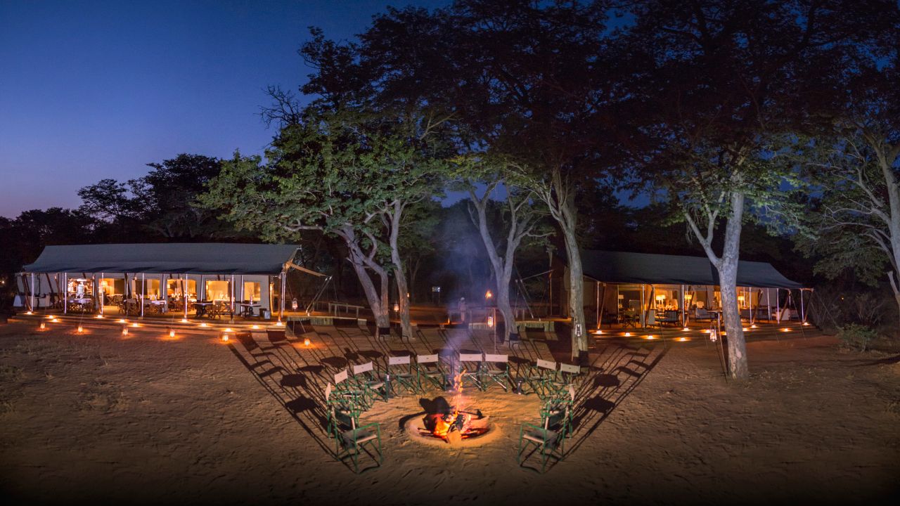 Elevated view of boma fire at night with lodge lit in background, Hwange