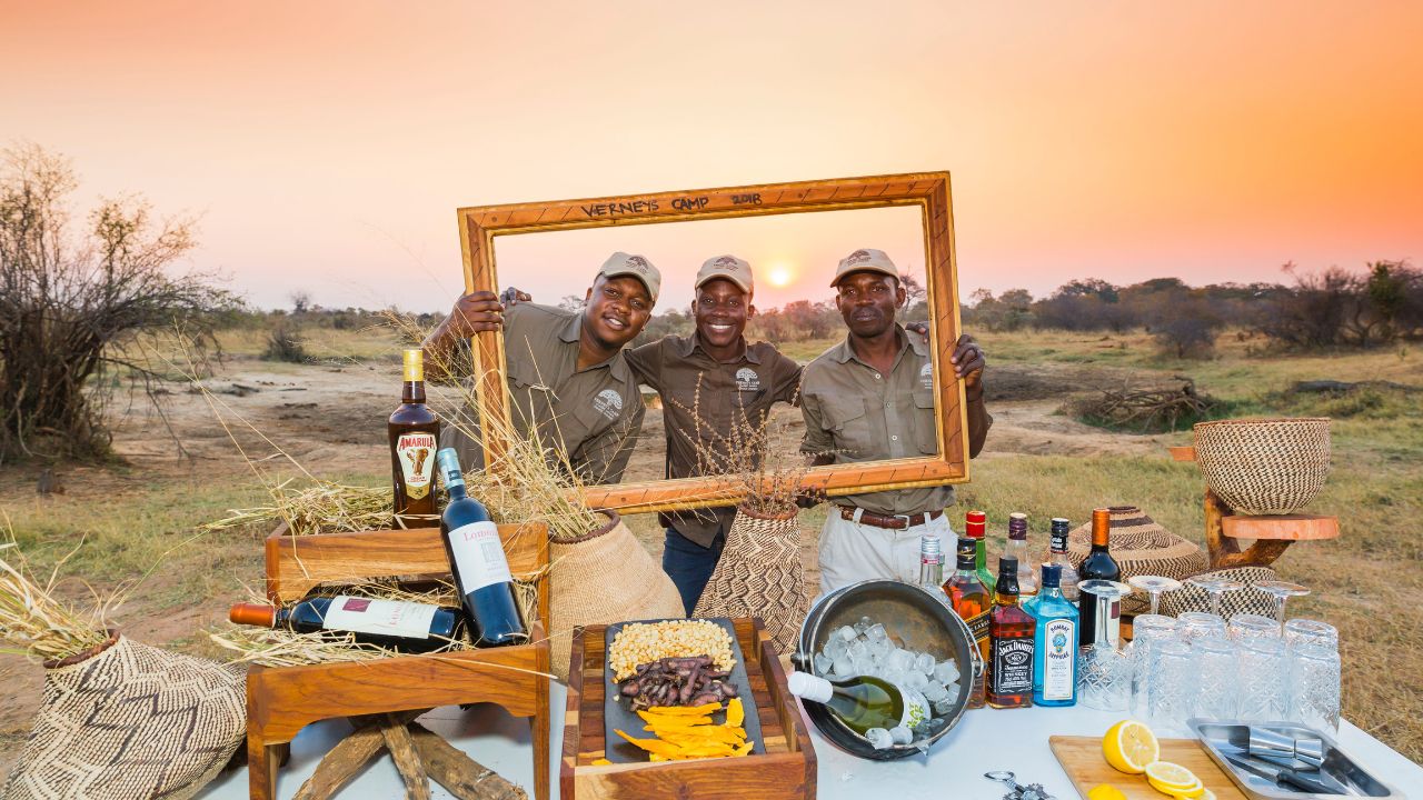 Rangers posing through picture frame at sundowner drinks setup, Hwange