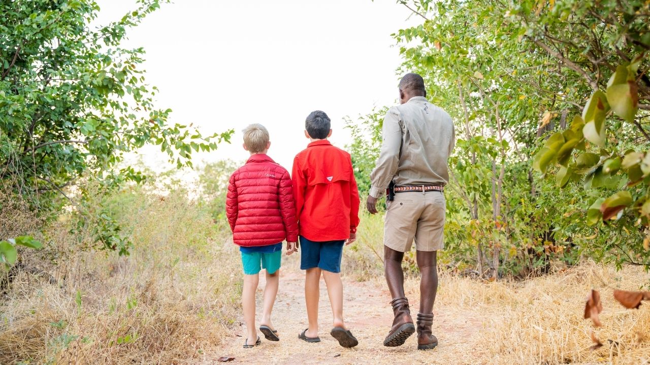 Two young boys walking with safari guide learning animal footprints