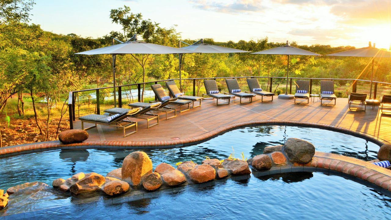 Victoria Falls Safari Club swimming pool at sunset with rocks and lounge chairs