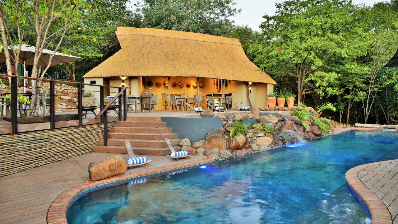 View from pool to Victoria Falls Safari Club main lodge with couple on deck
