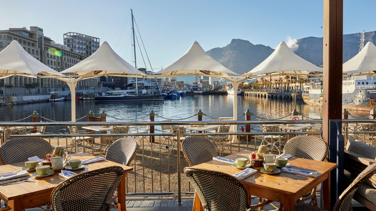 Outdoor tables at Queen Victoria Hotel with waterfront and Table Mountain view.