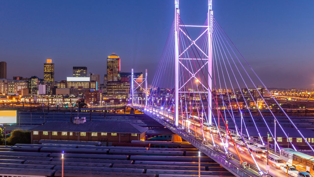 Nelson Mandela Bridge illuminated at night above Johannesburg railways.