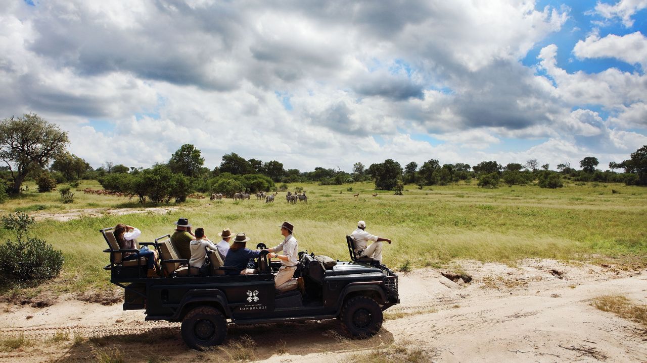 Safari vehicle in distance observing wildlife under cloudy sky at Londolozi, South Africa.