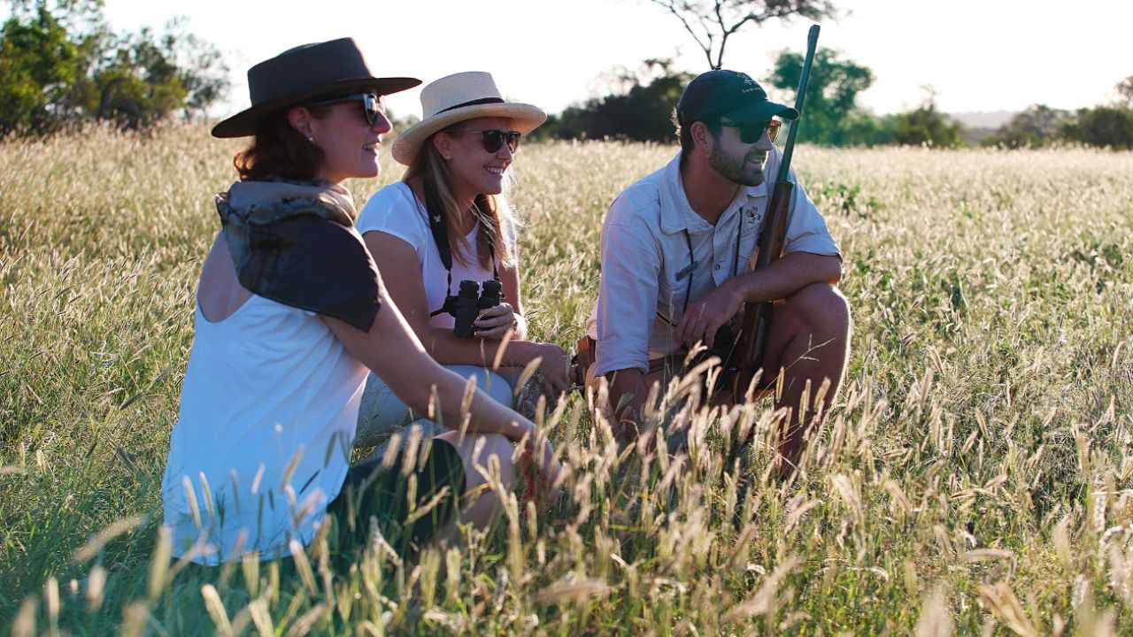 Game ranger and guests crouch in long grass during walking safari at Londolozi.