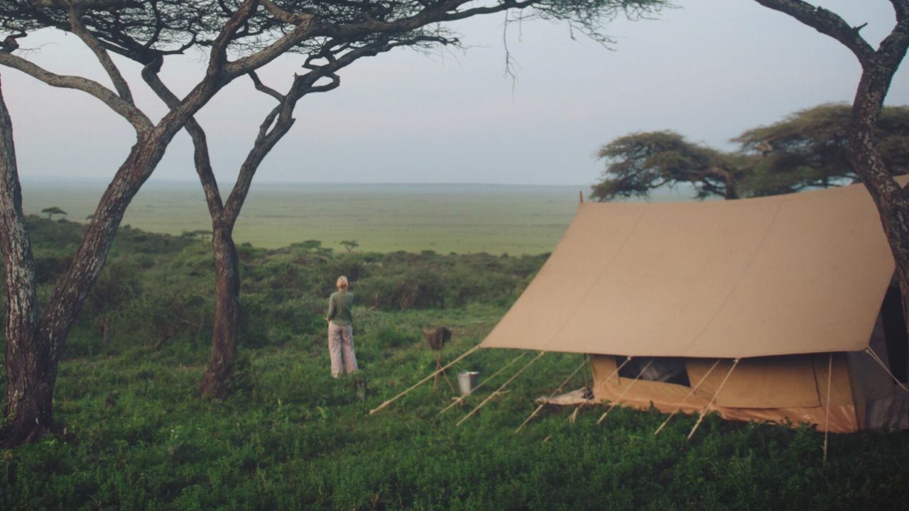 Guest standing near her safari tent overlooking the lush green Serengeti landscape.