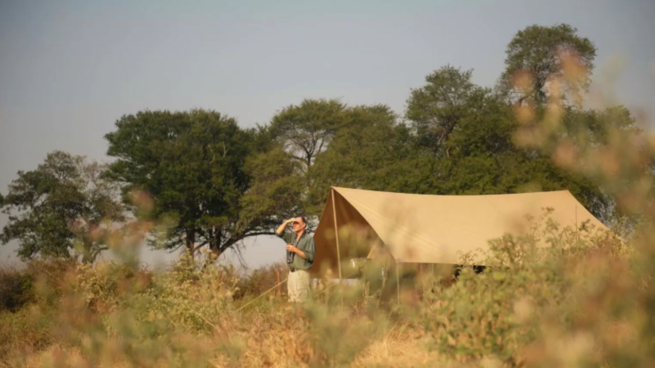 Guests stepping out of a canvas safari tent in the Serengeti bush, viewed from below.