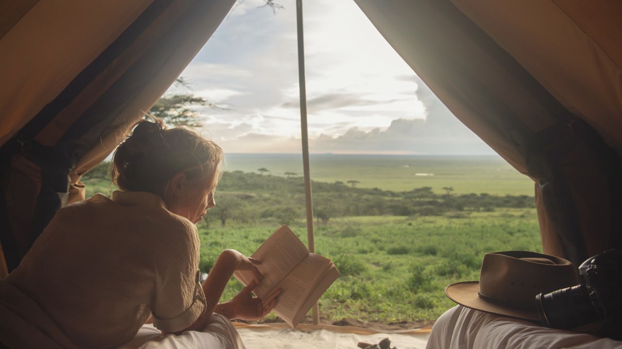 Guest reading inside a luxury safari tent overlooking the vast Serengeti plains in Tanzania.