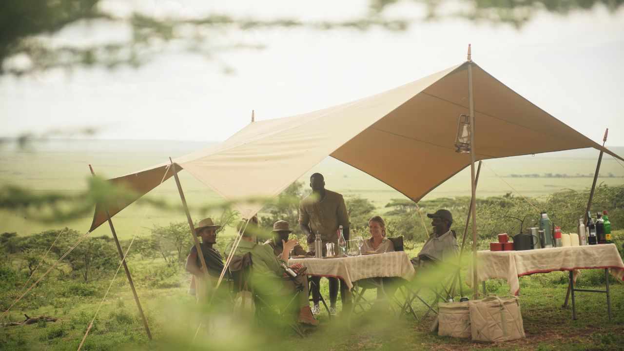 Rustic communal dining tent at Charlie Southwest Serengeti with guests enjoying an authentic bush dining experience.