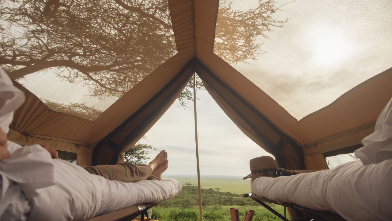 Guests relaxing on a safari bed with open tent front overlooking the Serengeti plains.