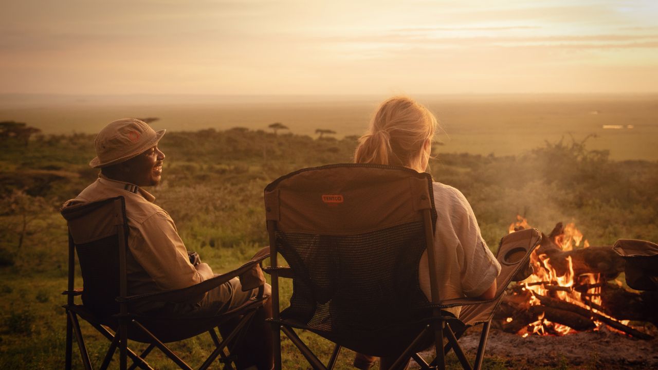 Guests and safari rangers enjoying sundowner drinks as the sun sets over the Serengeti.