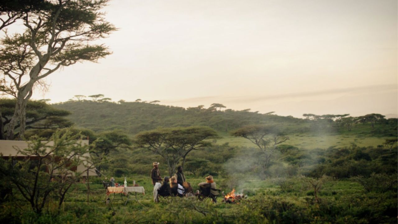 Guests and safari guides enjoying sunset dinner around a campfire in the Serengeti.