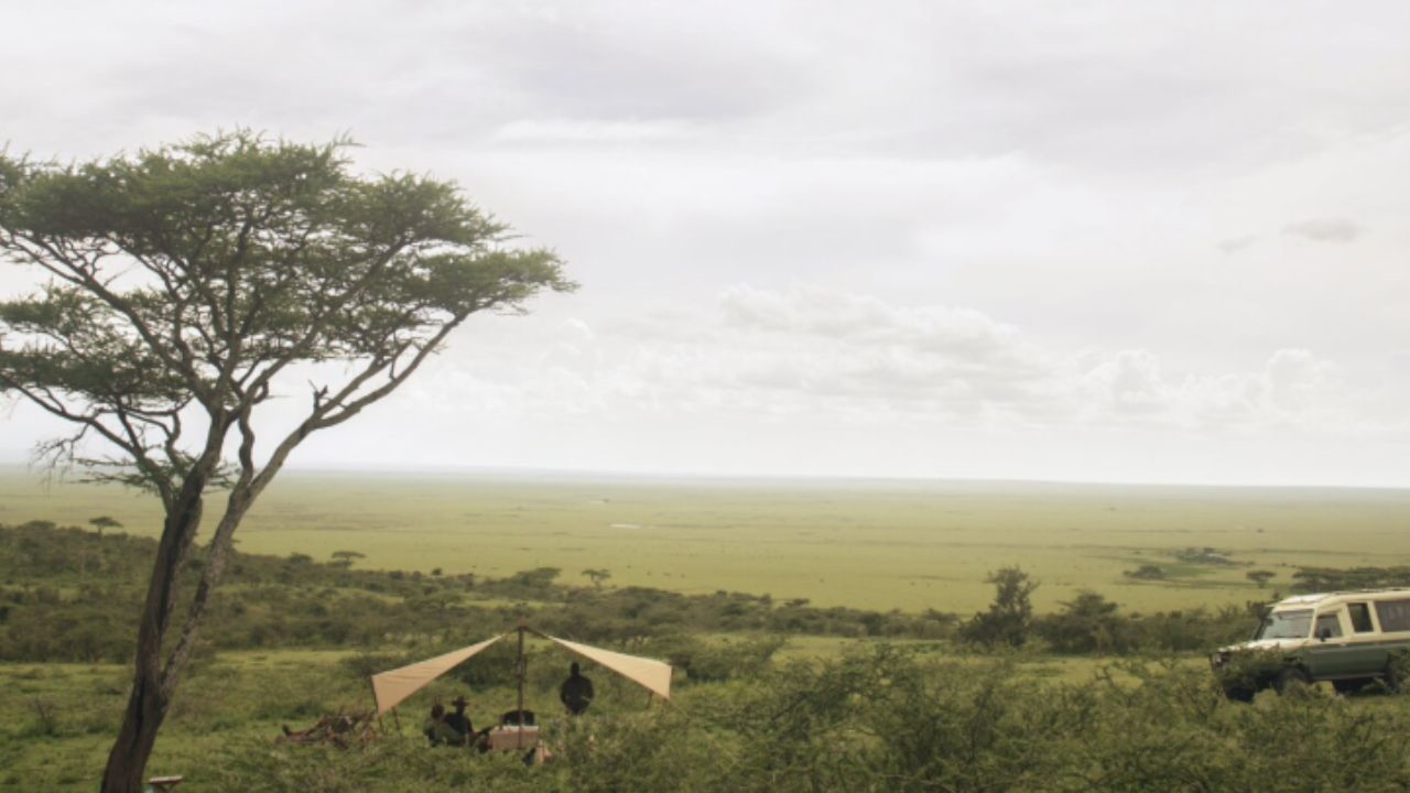 Tented dining area in the Serengeti with guests seated and vast plains stretching into the distance.