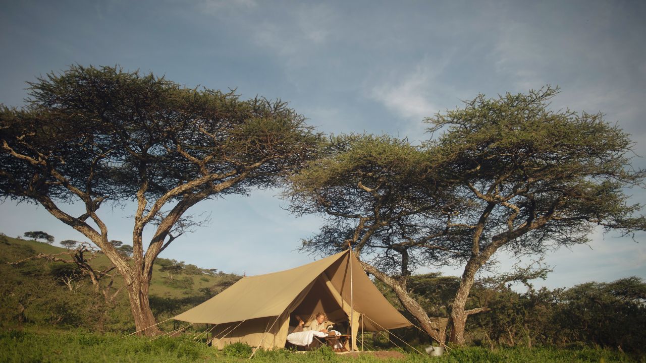 Canvas safari tent at Charlie Southwest Serengeti with guests relaxing inside reading books in the African bush.