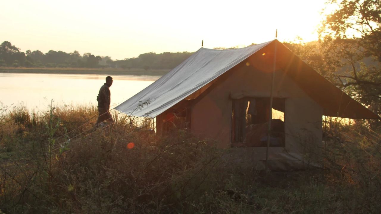 Safari guide walking past tented accommodation with river in the background, Tanzania.
