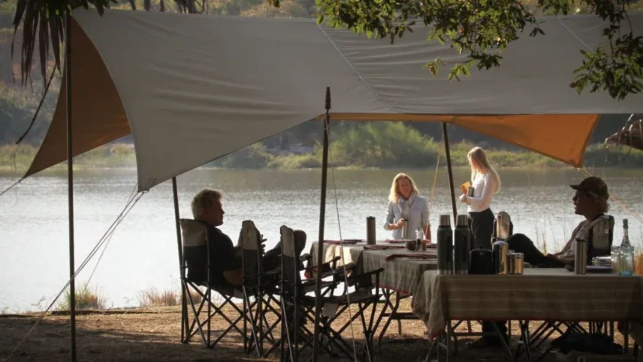 Guests enjoying communal dining under a tent with views over the river in Tanzania.