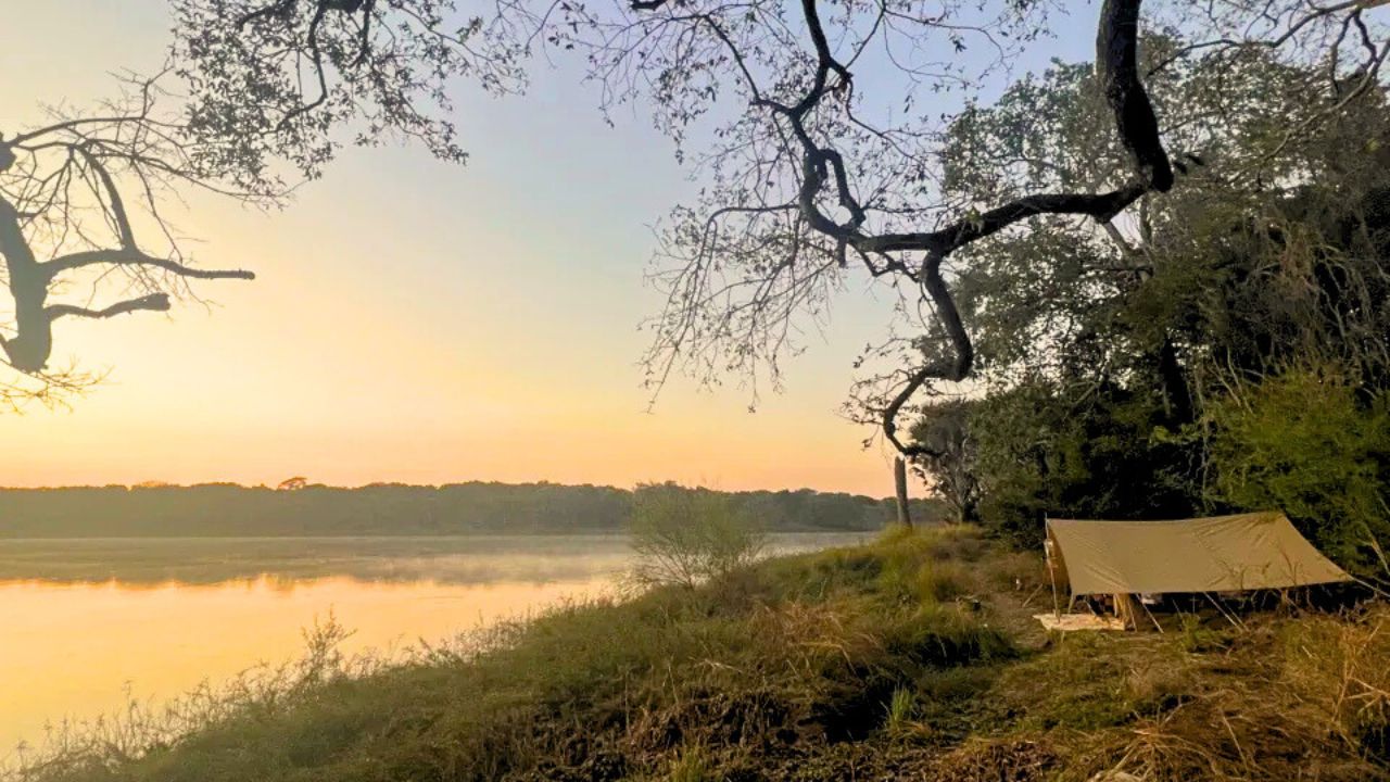 Canvas tent accommodation alongside a river at sunrise in Tanzania.