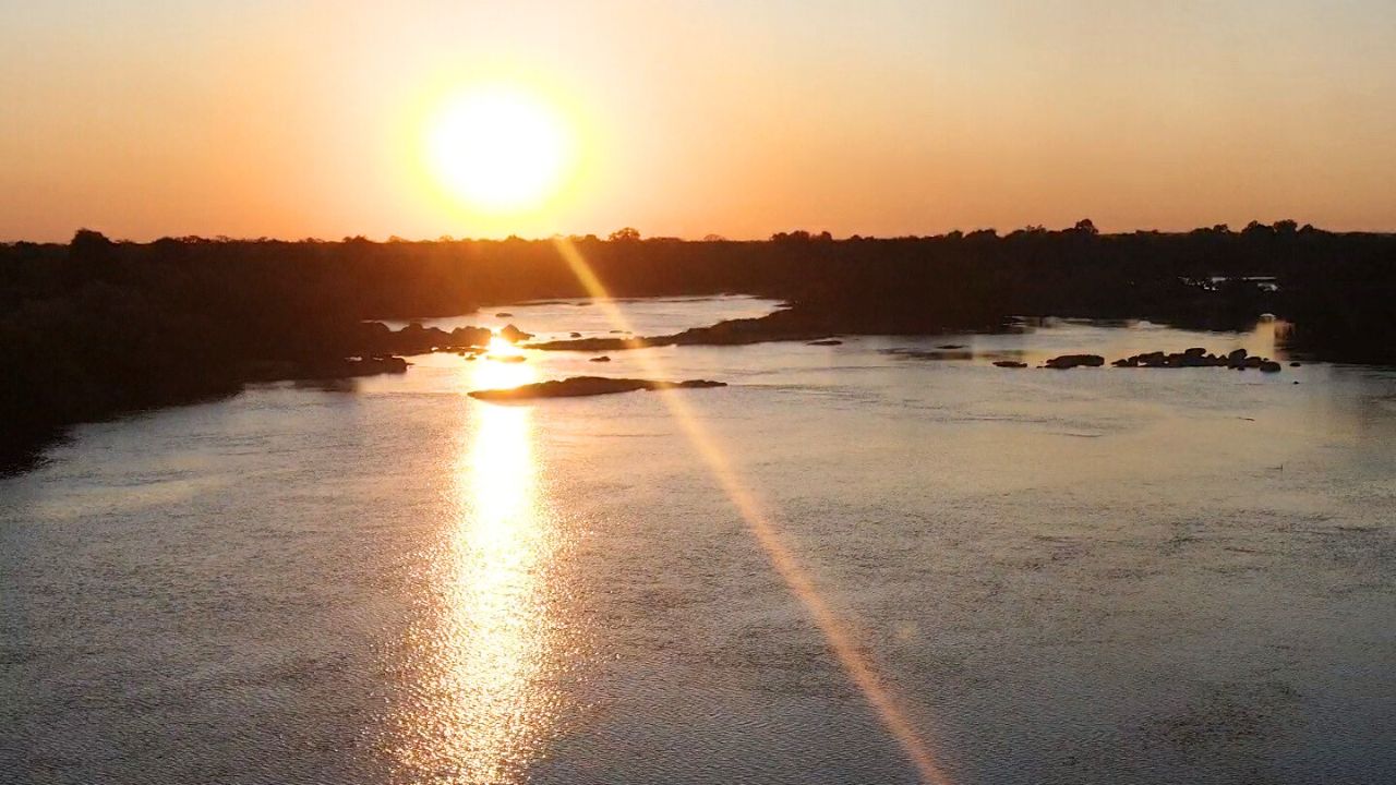 Sunset over Zambezi River, Zambia, with vibrant sky and calm water.