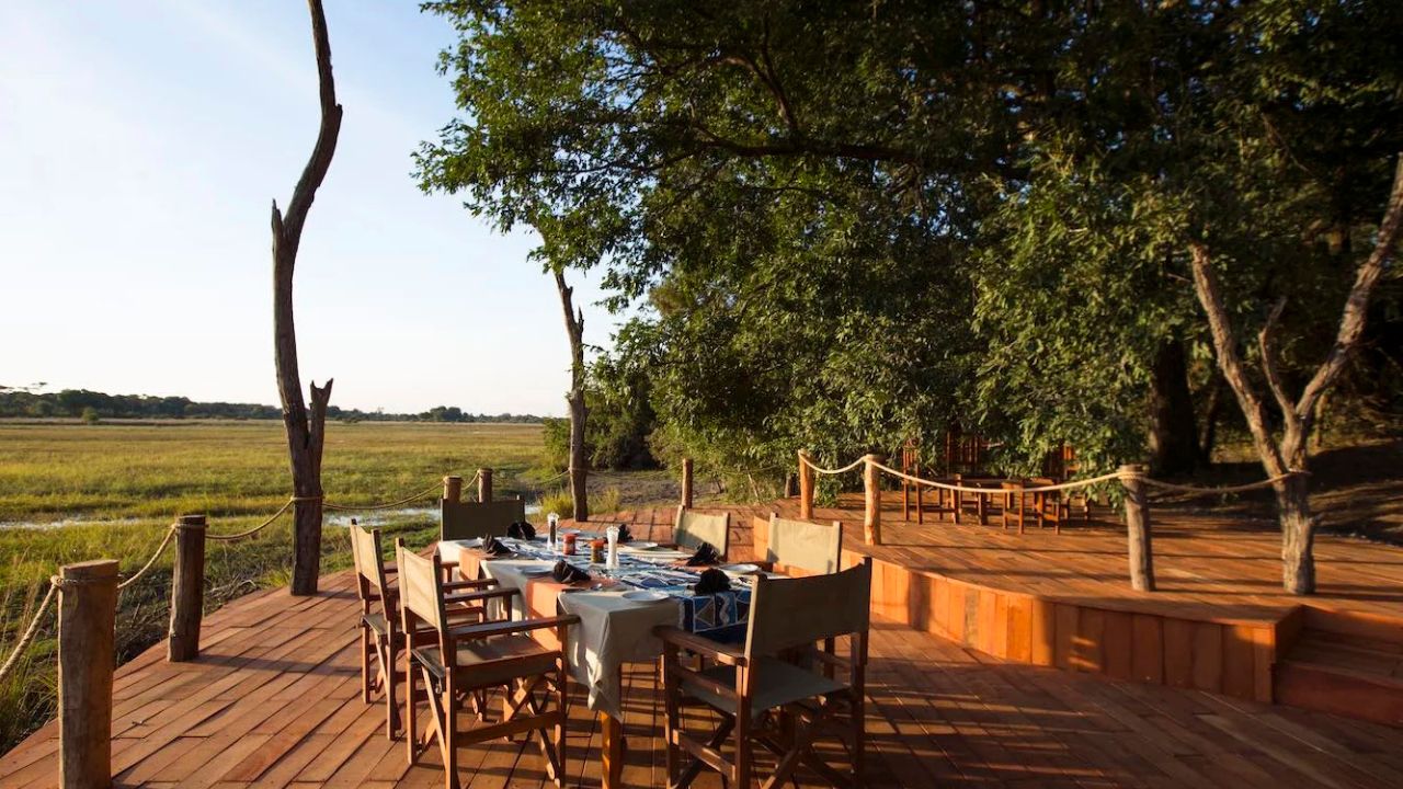 Daylight view of guest deck at Musekese Camp, set for breakfast with bush in the background.