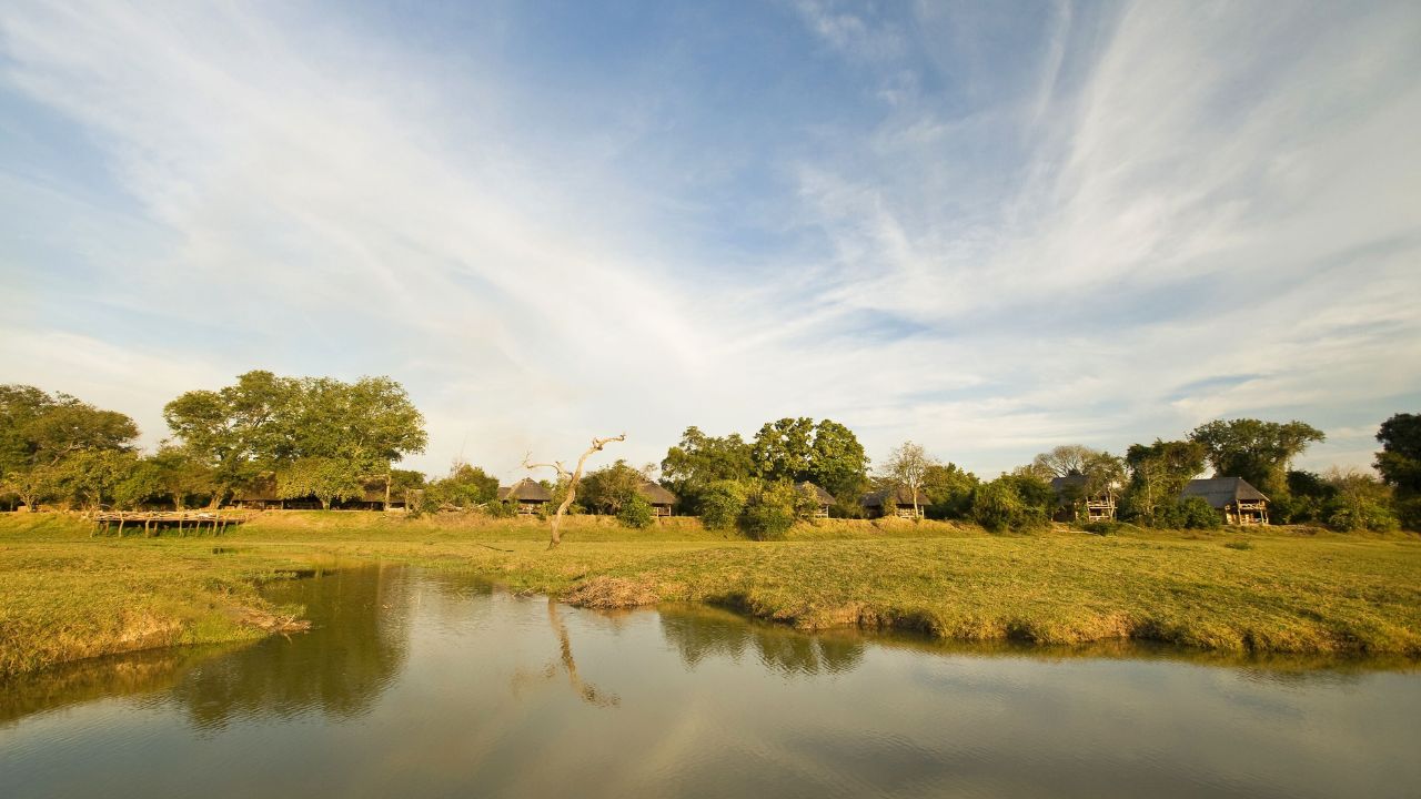 Wide-open view of Kafunta River Lodge across green water plains, lodge visible in background.