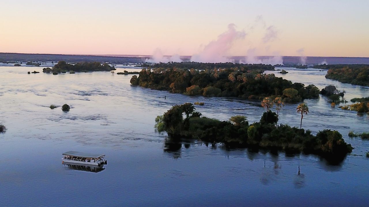 Aerial view of Zambezi Royal cruising Zambezi River with Victoria Falls smoke.