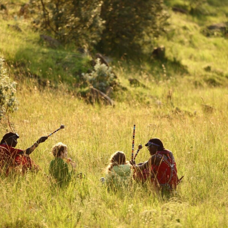 Kenyan guides leading children on walking safari in bush.