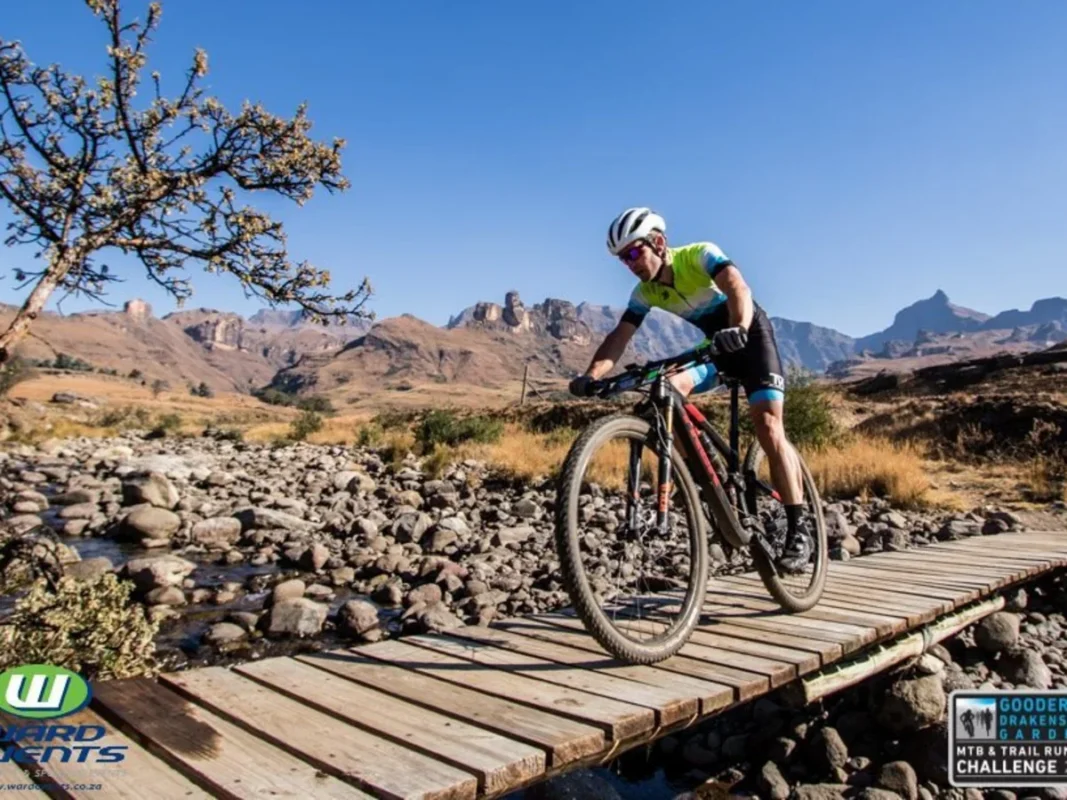 Mountain biker crossing bridge with Drakensberg Mountains in background.
