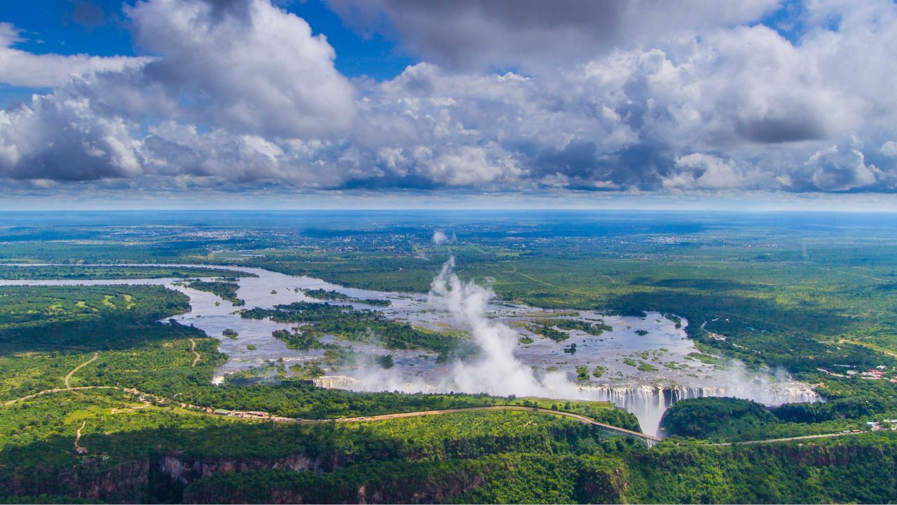 Victoria Falls in peak summer with lush green vegetation surrounding the Zambezi River.